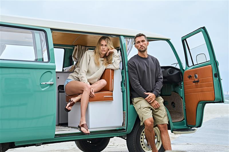 Frau und Mann in Tee Jays Label Free Kleidung neben einem Retro-Van am Strand.