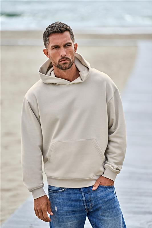 Mann in einem beigefarbenen Tee Jays Label Free Hoodie am Strand.