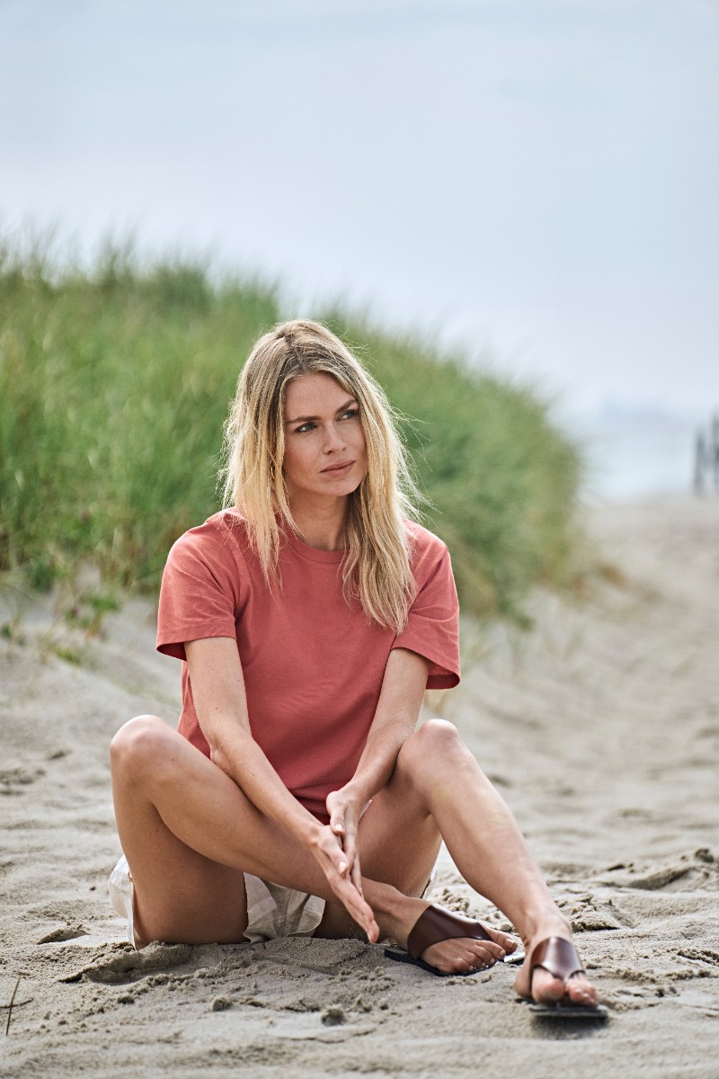 Frau im roten Tee Jays Label Free T-Shirt sitzt am Strand.