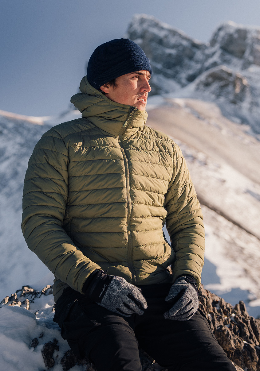 Man in an olive quilted jacket in a snowy mountain landscape.