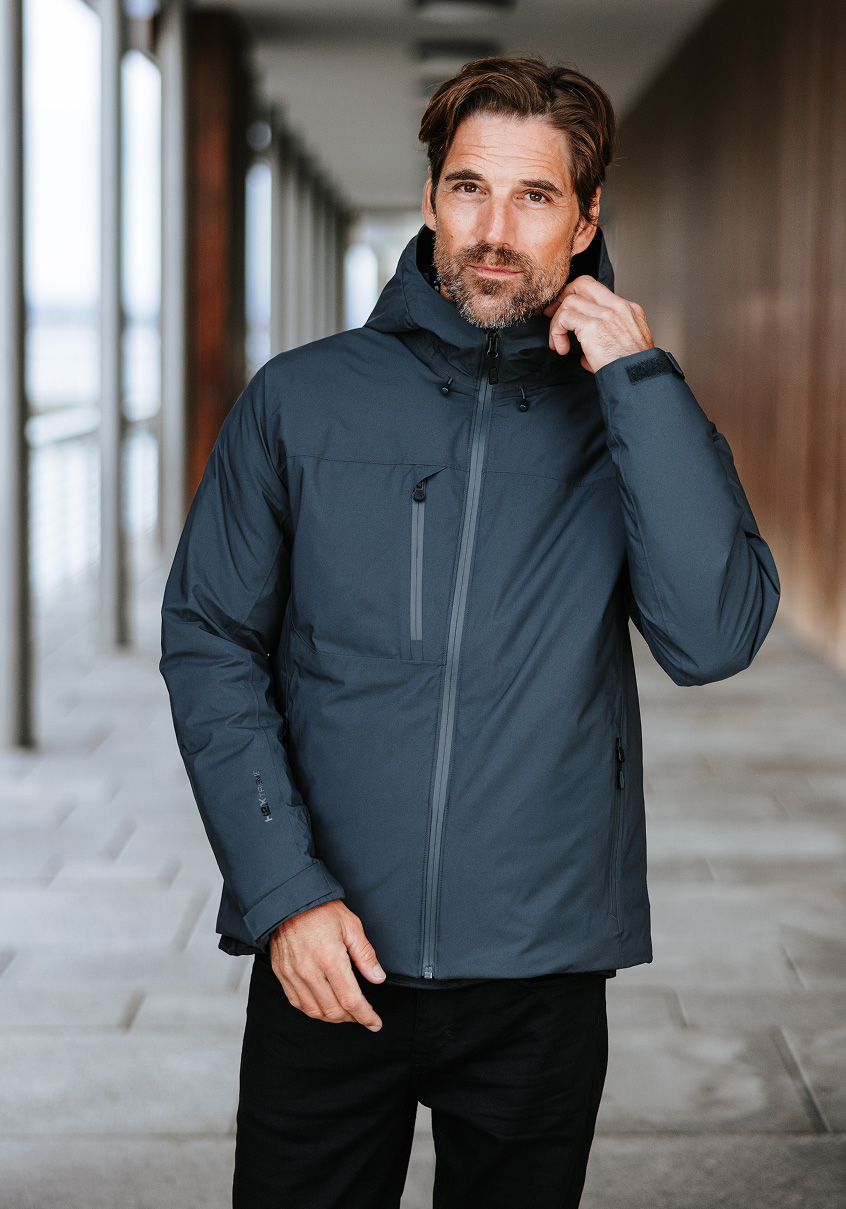 Man in a grey thermal jacket standing in a modern corridor.